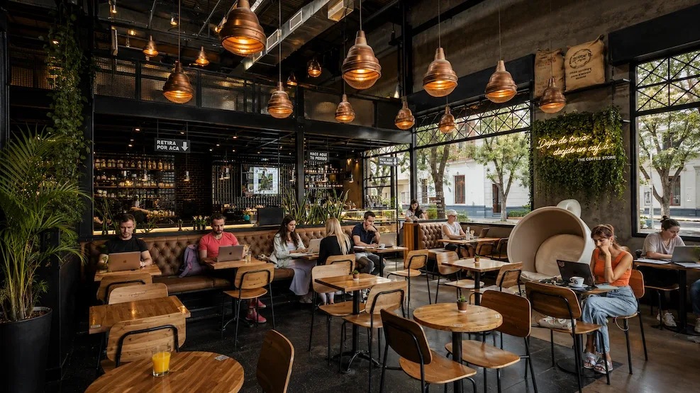 A packed café workspace in Palermo, laptops open under copper pendant lamps