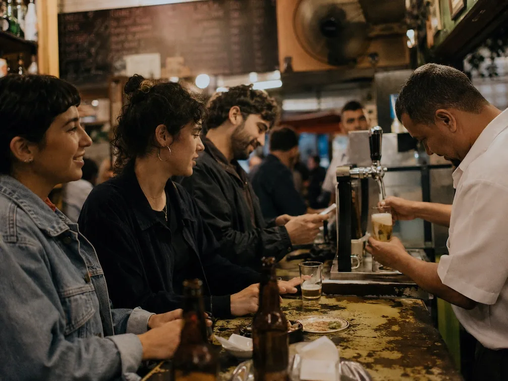 Friends at the counter of a São Paulo boteco while the bartender pours a chopp