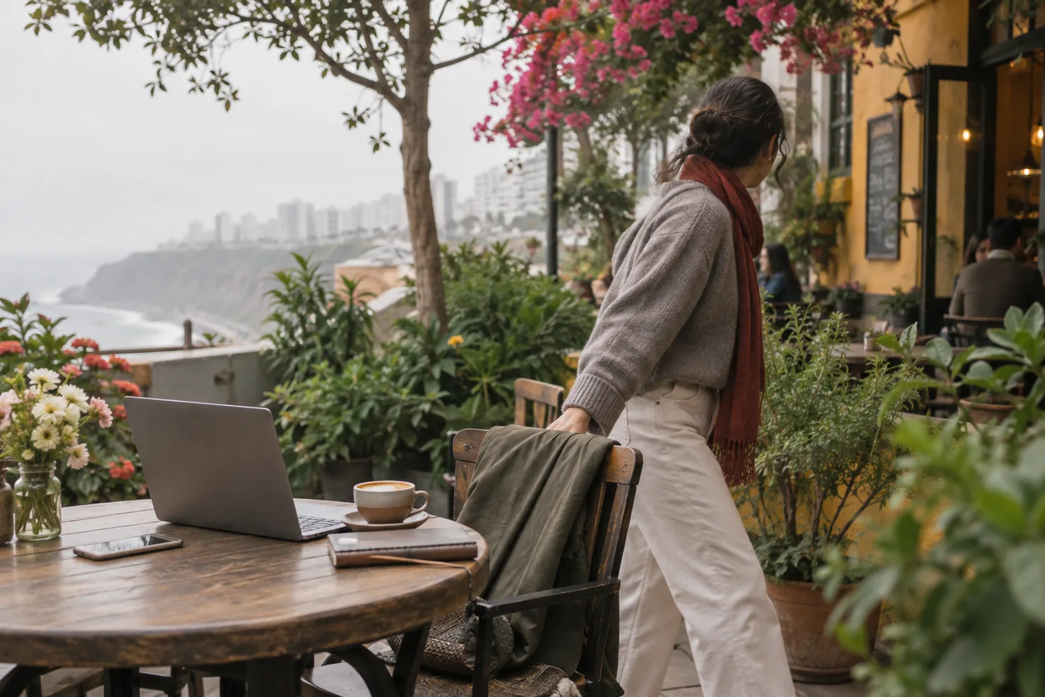 A garden café in Barranco under flat gray winter light, a laptop on the table and a jacket over the chair