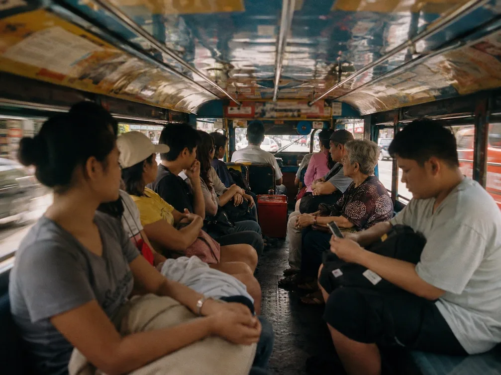 The interior of a Manila jeepney, passengers seated along both benches under a painted roof