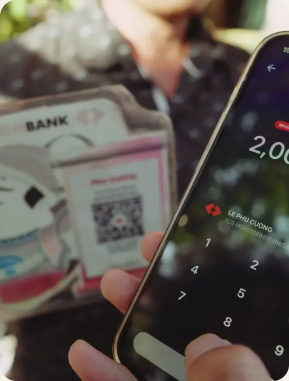A phone showing a VND payment amount held next to a Techcombank QR code card at a street stall.